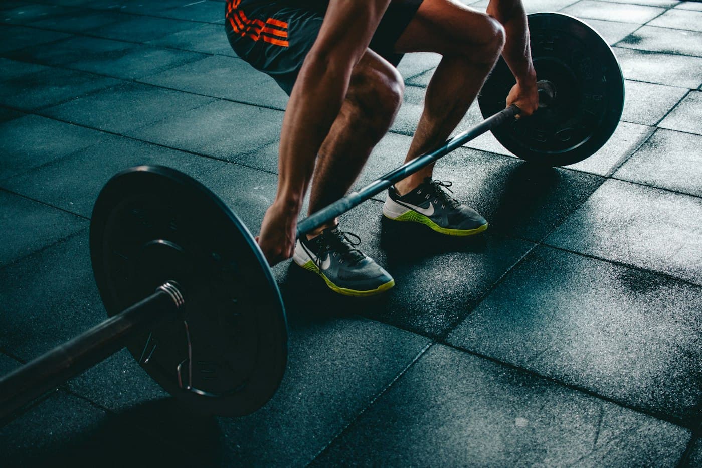 Person kneeling on a gym floor beside a dumbbell